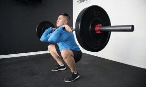 a man in a black and white room performing a full squat with a loaded barbell supported in a front rack position
