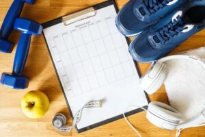 a pair of dumbbells, workout shoes, measuring tape, headphones, and workout plan outline