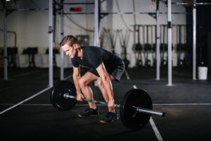 a man leaning forward and preparing to deadlift a loaded barbell in a gym