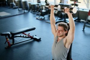 a man sitting on an upright gym bench and performing an overhead shoulder press