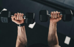 two hands holding a pair of dumbbells in a gym environment
