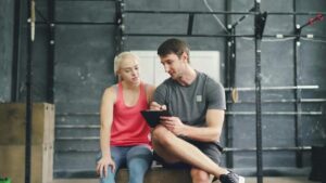 a man and a woman sitting on a plyo box in the gym and discussing a workout program